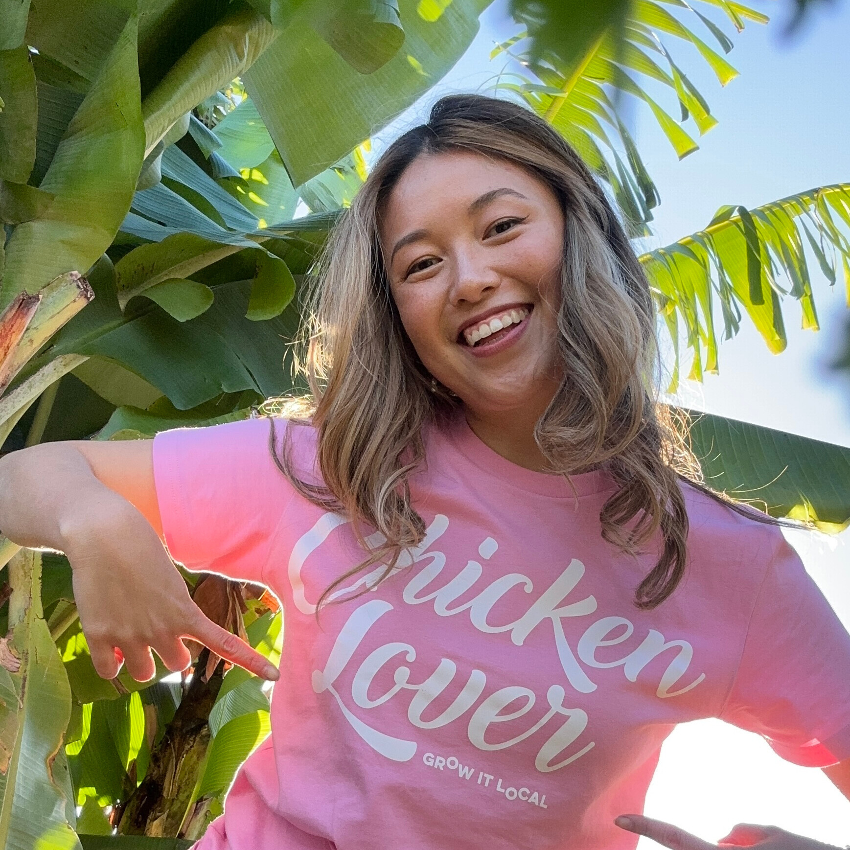 Smiling woman in pink 'Chicken Lover' shirt outdoors.