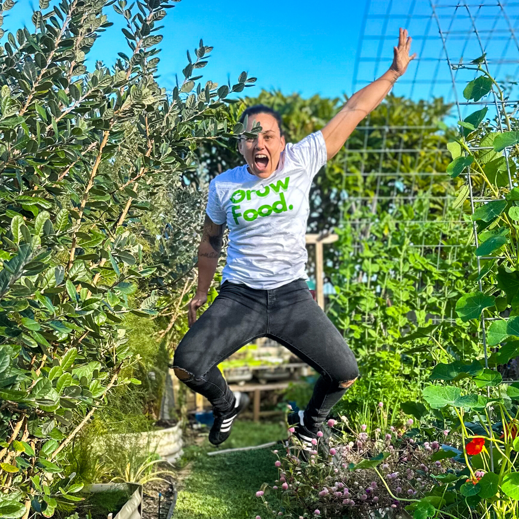 Person jumping in garden wearing 'Grow Food' shirt.