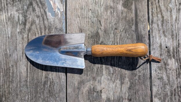 Gardening hand trowel on wooden surface.