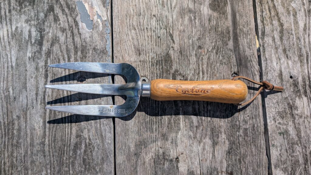 Wooden handle stainless steel gardening fork on timber surface.