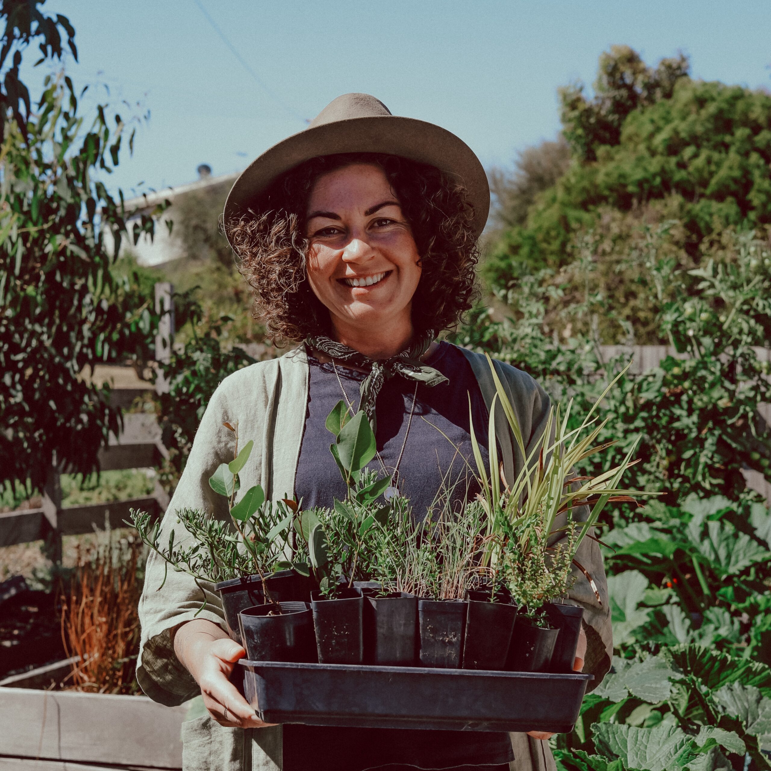 Smiling woman holding plants in a garden.