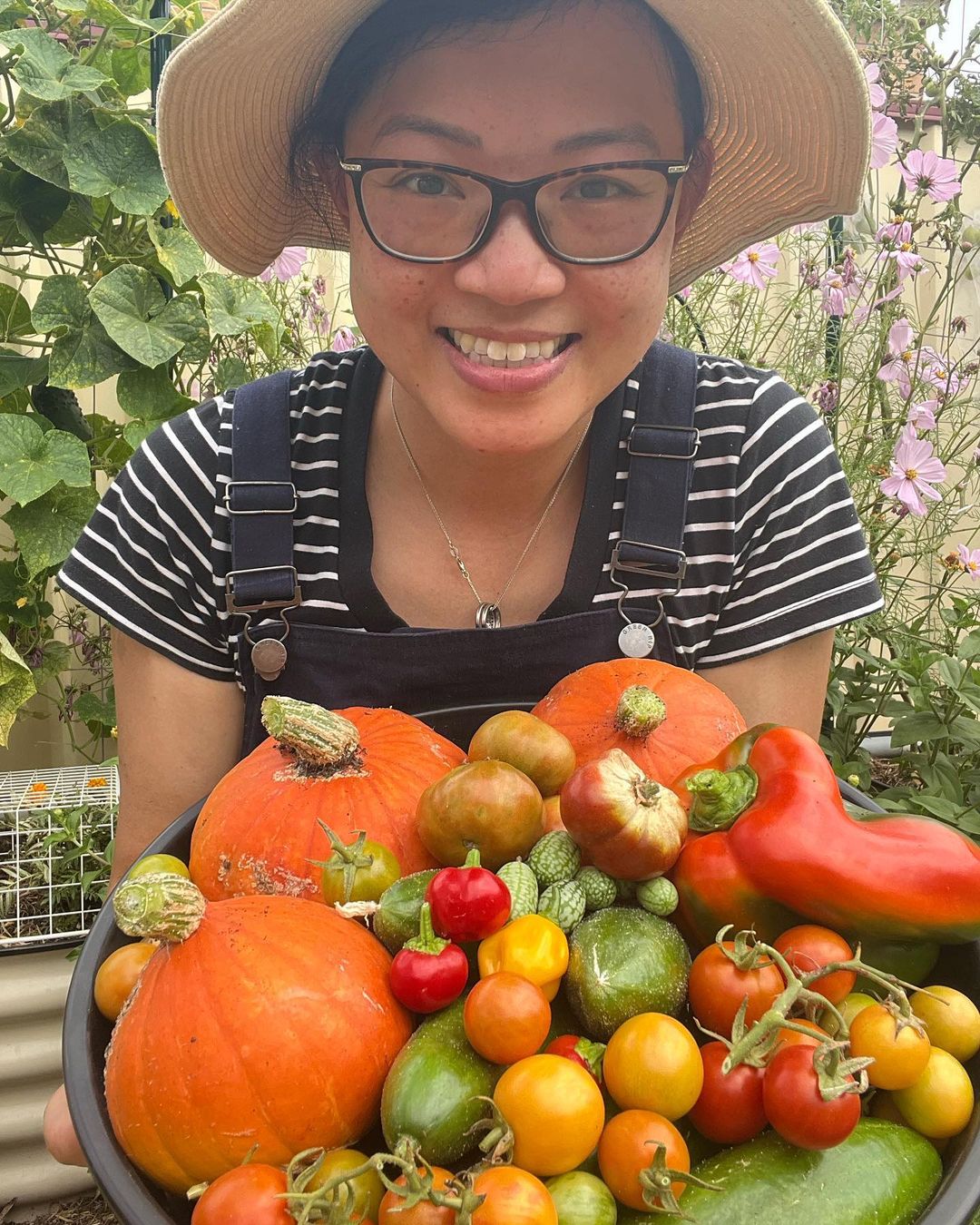 Gardener holding basket of colourful vegetables in garden.