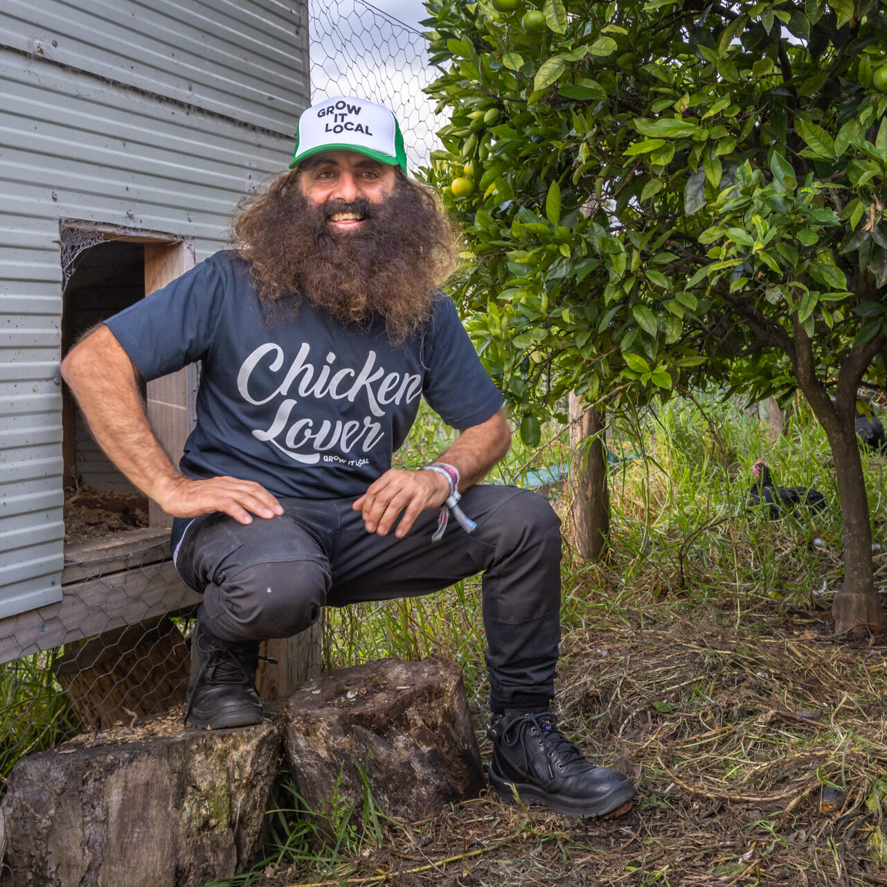 Man with beard near chicken coop and orange tree.