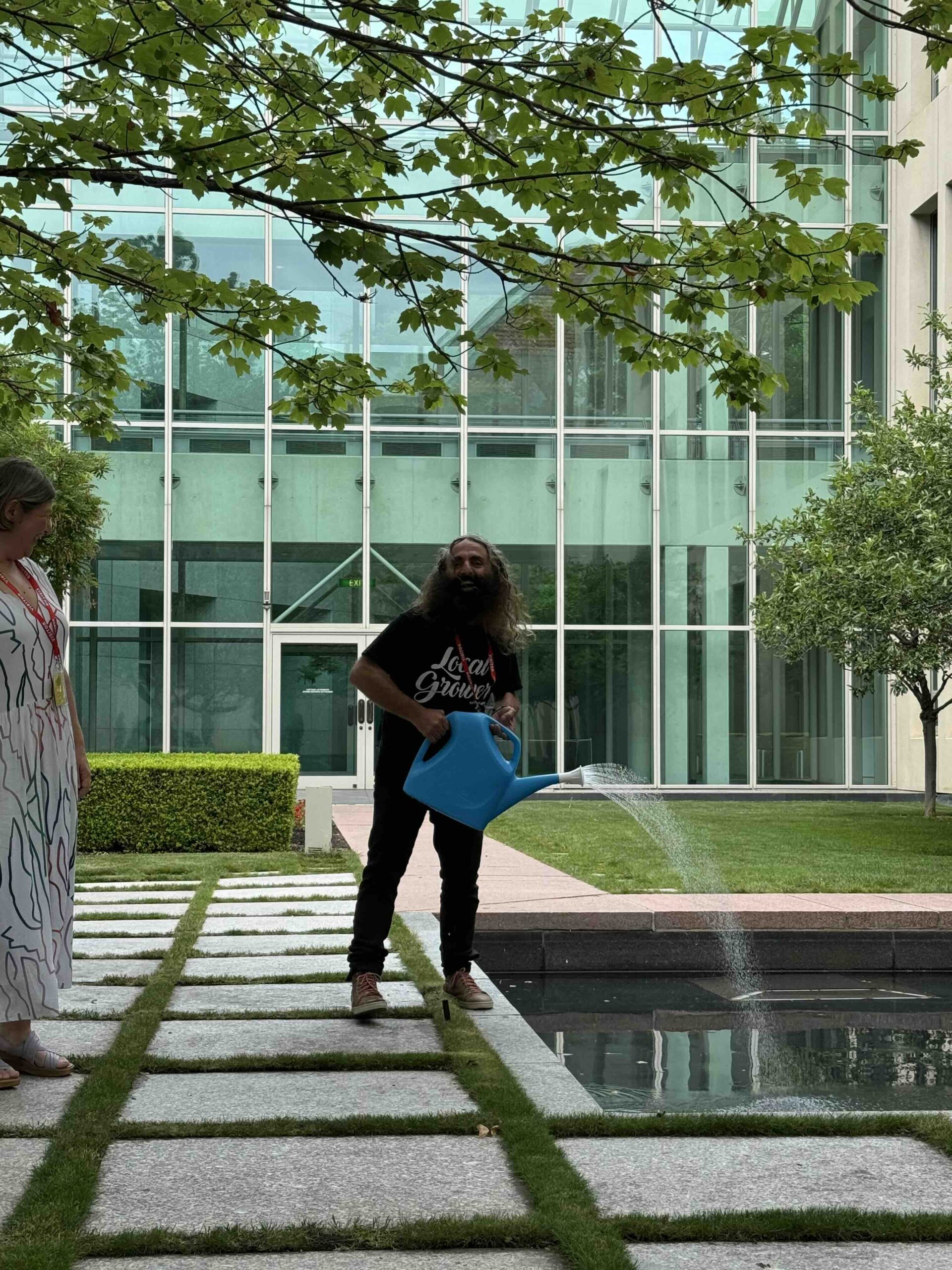 Man watering garden near modern building.