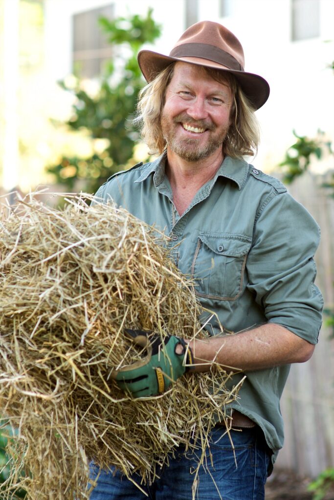 Phil Dudman in hat carrying straw outdoors.