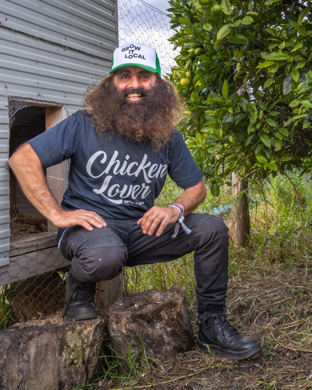 Man kneeling by chicken coop in garden.