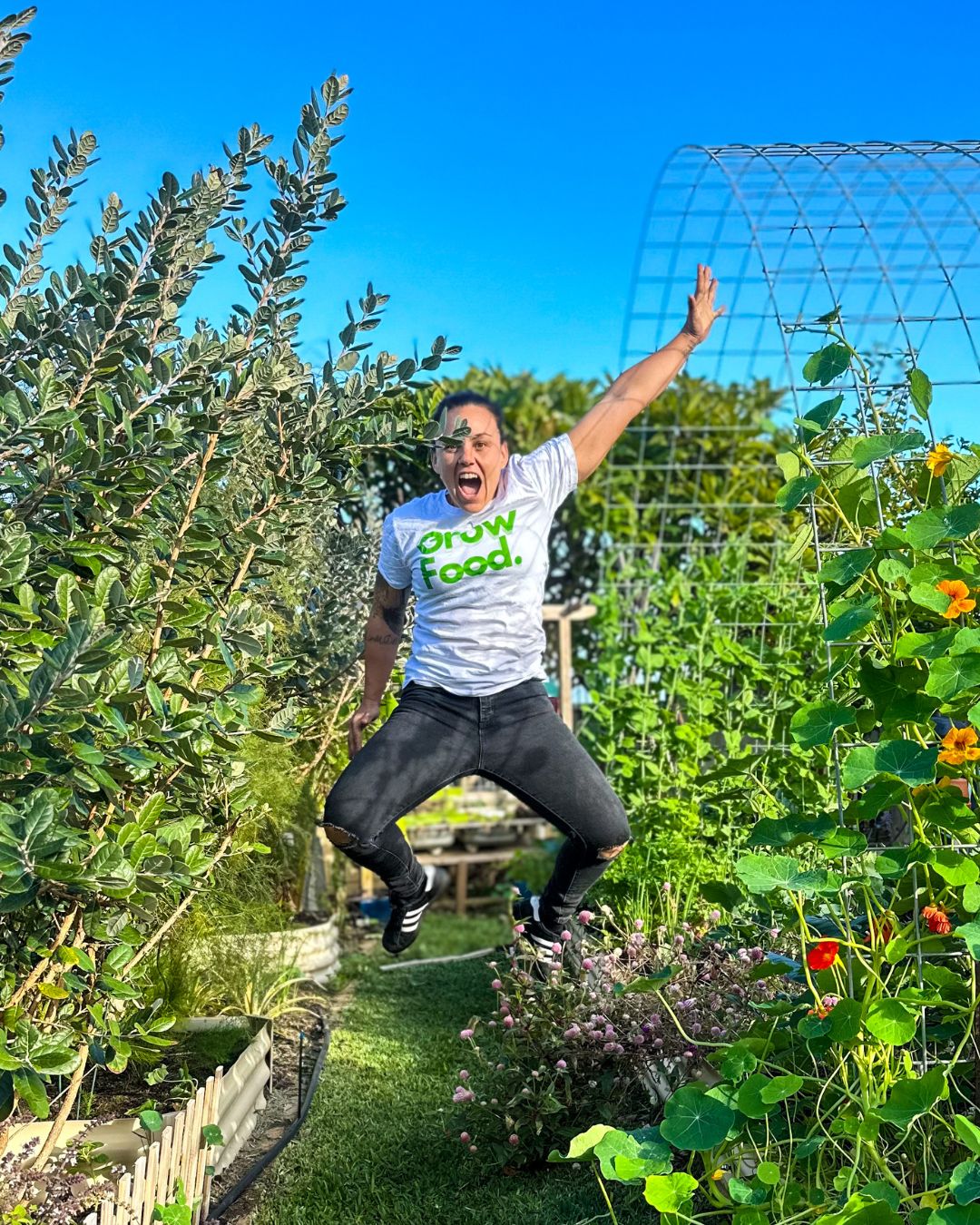Person jumping in lush garden, wearing Grow Food shirt.