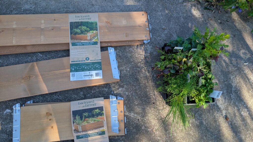 Garden bed kit and plants on concrete ground.