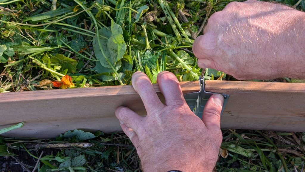 Building garden bed with hands and screwdriver.