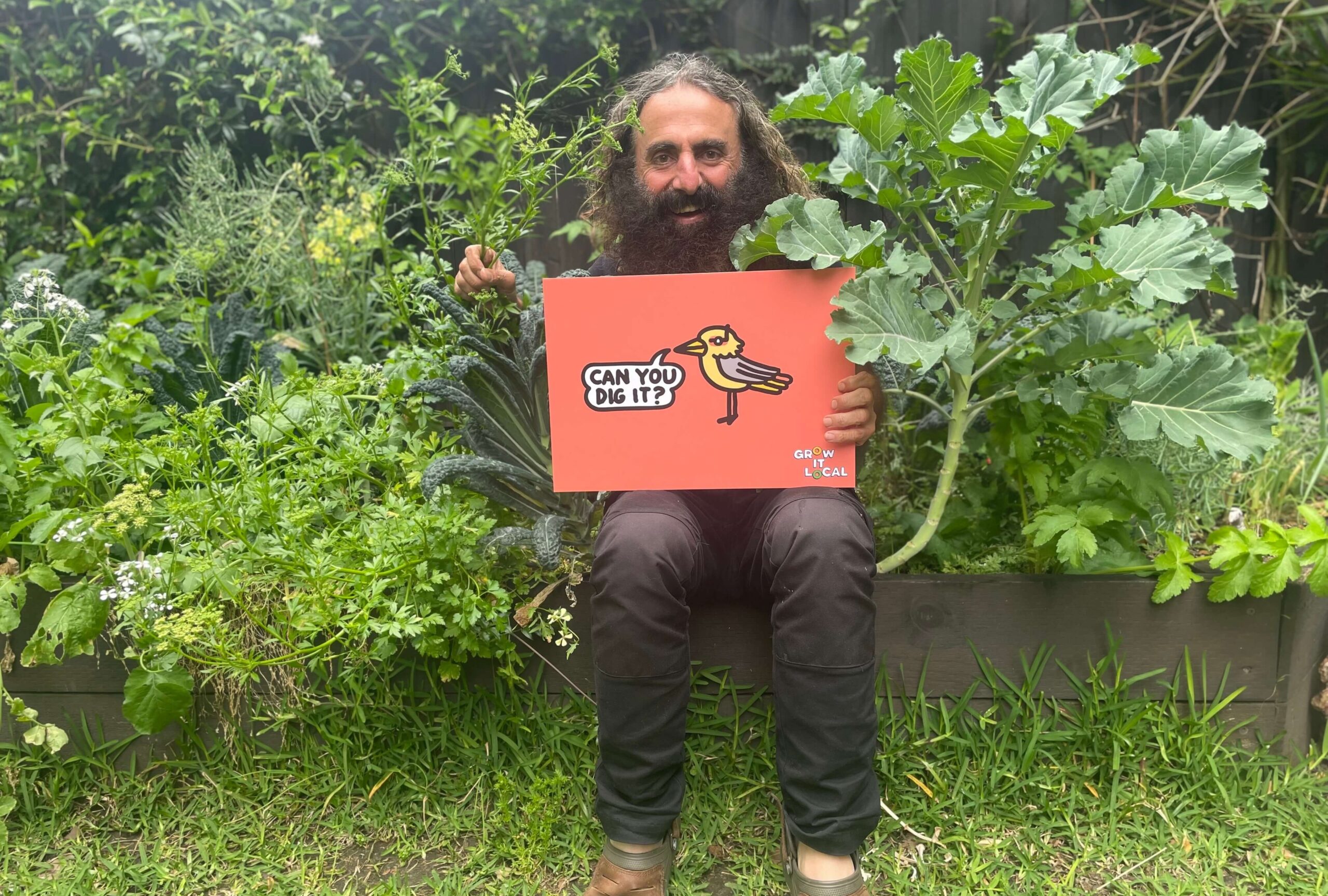 Man in garden holding 'Can You Dig It?' sign.