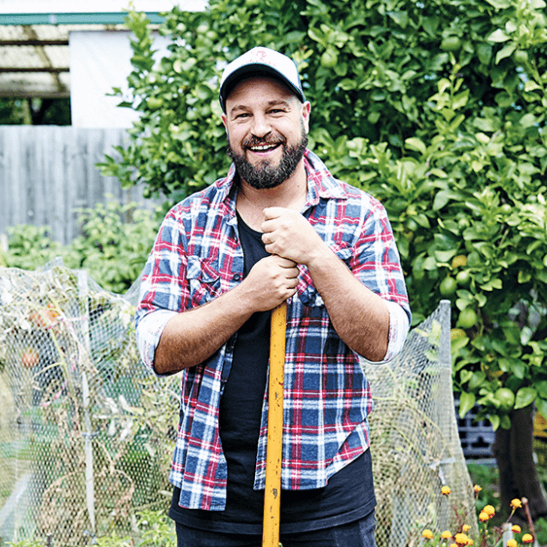 Man smiling in garden holding a spade.