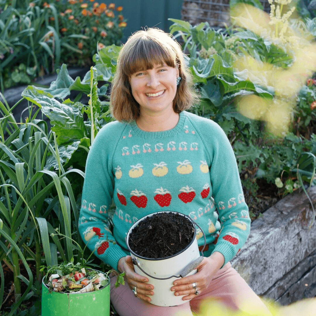 Smiling woman gardening with compost bucket.