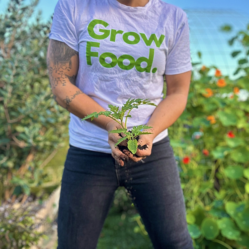 Person holding seedling, 'Grow Food' shirt, garden background.
