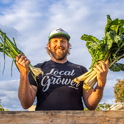 Man with harvested greens and onions, smiling outdoors.
