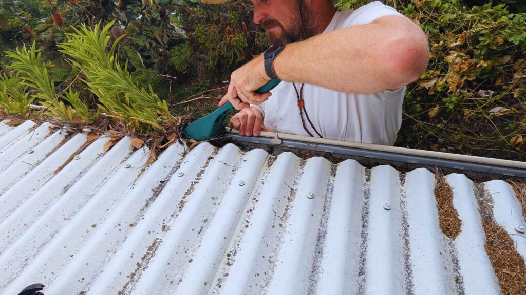 Man cleaning roof gutters with a scoop tool.