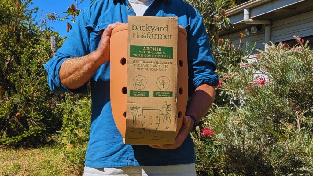 Person holding terracotta worm composter in garden